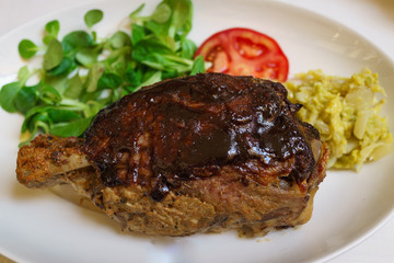 knuckle of traditional italian baked pork leg with vegetable, tomato and potatoes on white dish