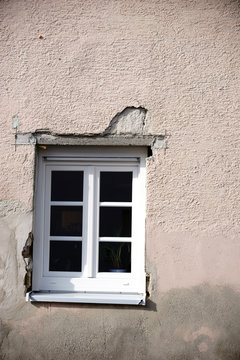 Neu eingesetztes Fenster  / Die Fassade eines renovierungsbedürftigen Hauses mit neu eingesetztem Fenster.