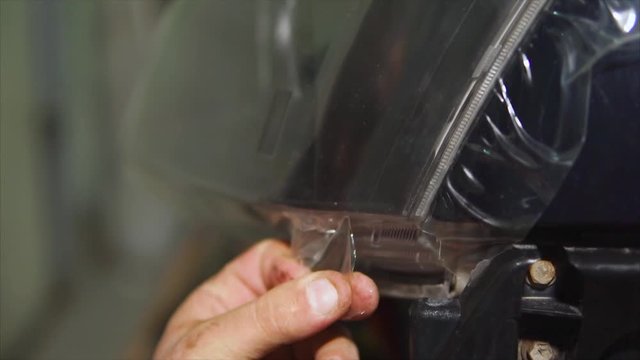 Close up shot of the car expert hands who tear off the vinyl film on the headlights of blue expensive car. This film protects the vehicle from the small chips and scratches.