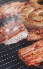 Grilled sausage and pork cooking with smoke on flaming grill.