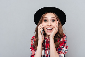 Cheerful young woman standing over grey wall talking by phone.