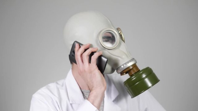 Man in a lab coat wearing a gas mask talking on the phone