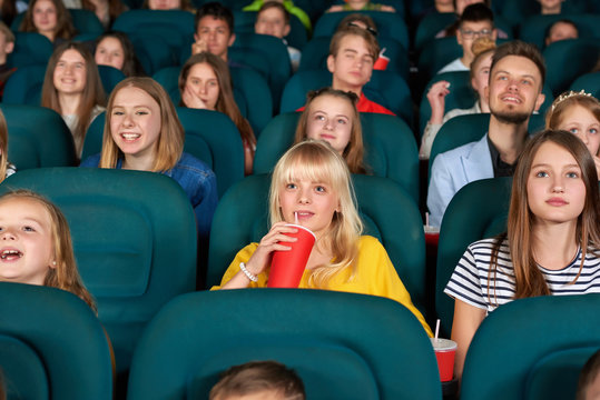 Beautiful young girl smiling drinking coke at the movie theatre enjoying watching film with her friends and classmates children people entertainment comfort weekend holidays concept.