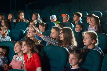 Young girl laughing pointing at the screen while watching a movie at the local cinema children...