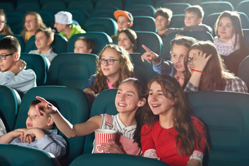 Two young girls smiling joyfully enjoying watching a movie together at the cinema friends friendship entertainment activity holidays weekend childhood happiness positivity comedy concept.