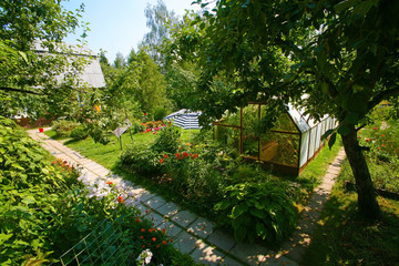 Garden with blossoming flowers, the house, hothouse and trees