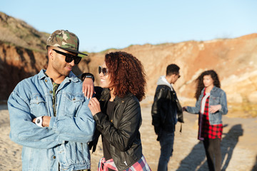 Smiling young loving couple walking at beach with friends