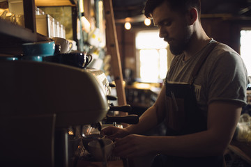 Young male barista preparing drink at coffee machine