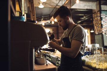 Young male barista preparing drink at coffee machine