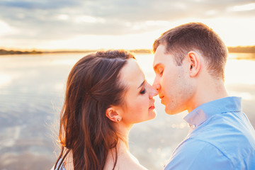 Obraz premium Young beautiful couple in love staying and kissing on the beach on sunset. Soft sunny colors.