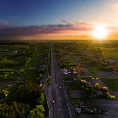 Aerial view of the motorway in the area of the village at sunset. The road from above on the sides of which the green fields and the village