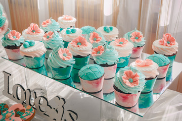 Close-up photo of wedding cupcakes placed on a glass stand on a dessert table at reception, pink-brown color palette