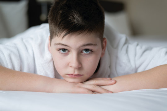 Boy in bathrobe lies in bed in hotel room