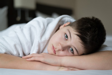 Obraz na płótnie Canvas Boy in bathrobe lies in bed in hotel room