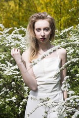 Blond girl in white dress among white flowers. Spring