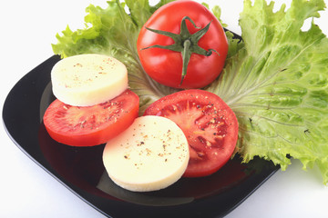 Portion of Mozzarella with Tomatoes, lettuce leaf and Balsamic dressing on black plate. selective focus close-up shot.