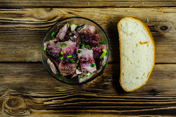 Herring with spices in glass bowl and sliced bread on wooden table. Top view