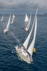 Coming fleet of sailing boats during offshore race passing yellow buoy, bird view angle