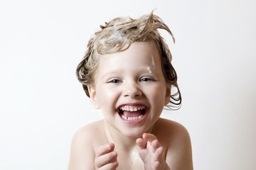 adorable little girl with blue eyes washing her hair in the bathroom and laughs, foam on the head, look at the camera