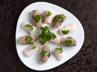 Rolls of ham and beef tongue on a white plate