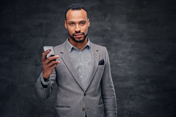 Portrait of elegant bearded black  male in a suit holds smart phone.