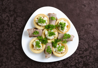 Rolls of tongue and tartlets with salad on a white plate