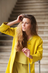 Young woman touching her hair, leans on the suitcase handle and looking in the distance
