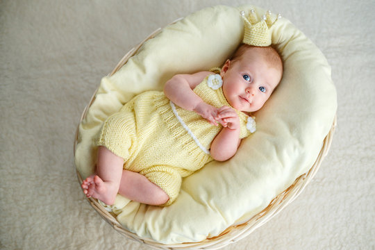 Newborn baby girl lying in a basket with crown and yellow bodysuit