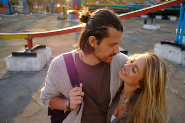 Happy smiling couple in love hug and kiss each other in the amusement park. Sunny warm spring evening