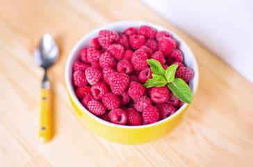 Raspberries in ceramic bowl. Ripe and tasty raspberries on a wooden background.