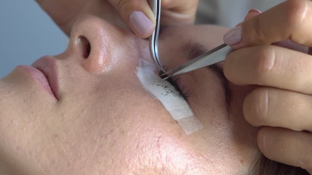 Professional master make long lashes holding out a pair of tweezers. Eyelash extension in beauty studio.