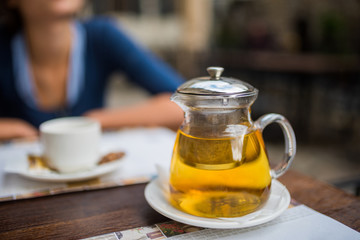 Pitcher of tee and a cafe table. Young woman in the blurred backgroung.