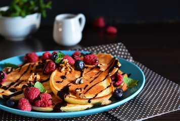 Vanilla pancakes with berries and chocolate sauce on a dark background
