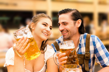 Young couple flirting in Oktoberfest beer tent while drinking beer