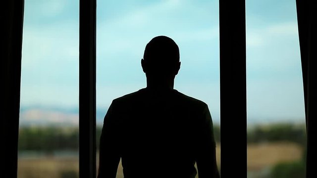 Young man opens big window curtains and lets the light in the room. Man opens the curtains in hotel room. Young man opens the curtains in the morning, raises his hands and stretch oneself