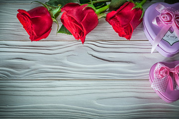 Heart-shaped metal gift boxes bloomed red roses on wooden board 