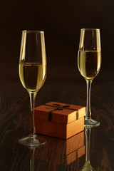 Two glass with white wine and gift box on mirror table. Celebrities composition. Selective focus.