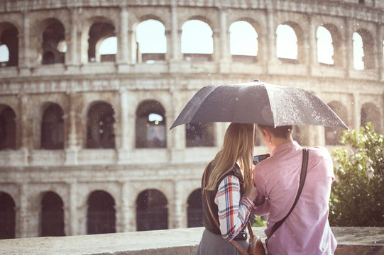 A couple with an umbrella in a rainy day, are taking pictures at the Great Roman Colosseum ( Coliseum, Colosseo ),also known as the Flavian Amphitheatre. Famous world landmark. Scenic urban landscape.