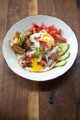Eggs over medium with a side of avocado, bacon, potato, and tomato 