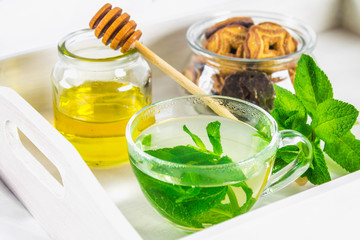 Mint tea in a cup, a jar of honey, a cookie in a jar, on a white tray in bed.