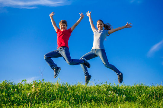 Two kids jumping together on green spring hills