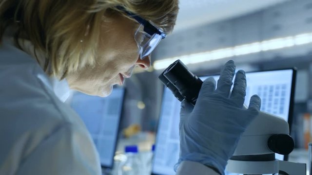 Senior Female Biologist Works on Her Computer and Looks at Materials under Microscope. She's in a Modern Laboratory. Shot on RED EPIC-W 8K Helium Cinema Camera.