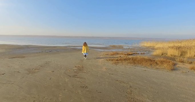 A young girl walks along the beach to the water, in yellow raincoat, a video shot from the drone.