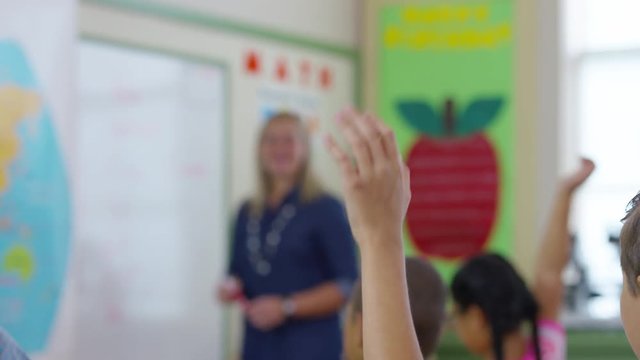 Teacher gives lesson in school classroom and students raise hands, rack focus