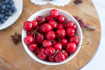 Cherry in the white bowl at the wood table. Fruit. Summer. Close up