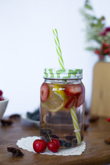 Glass jar with lemonade and green straw. Water with fruit, lemon, strawberry and blueberry. Cherry. Summer vibes