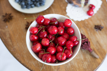 Cherry in the white bowl at the wood table. Fruit. Summer. Close up