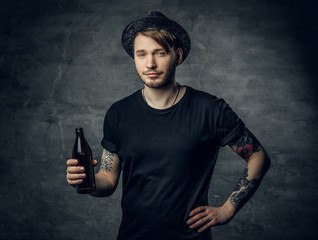 A man with tattooed arms holds craft bottled beer.