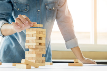Hand of engineer playing a blocks wood tower game (jenga) on blueprint or architectural project.