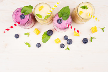 Freshly blended yellow and violet  fruit smoothie in glass jars with straw, mint leaves, mango...